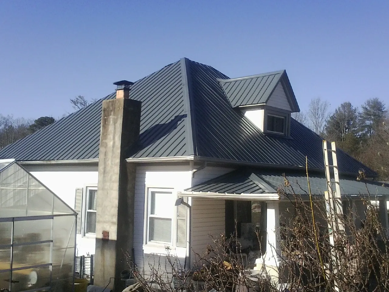 Dark blue standing seam metal roof on a white farmhouse with dormer — Slate & Tile Roof Repair by Roofing Brothers in Conifer