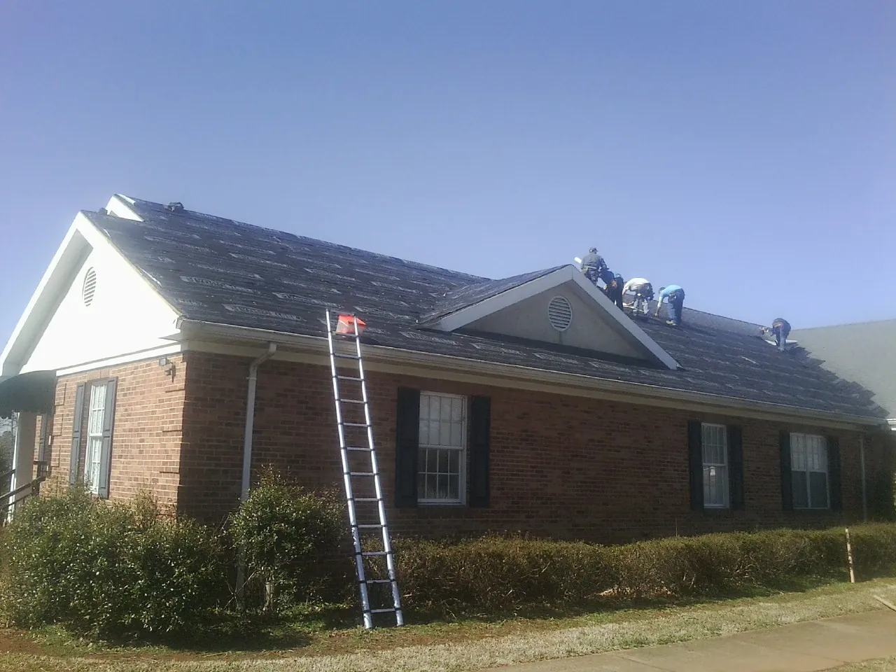 Crew tearing shingles off a brick ranch roof with a ladder set — Metal Roof Repair work by our crew in Conifer