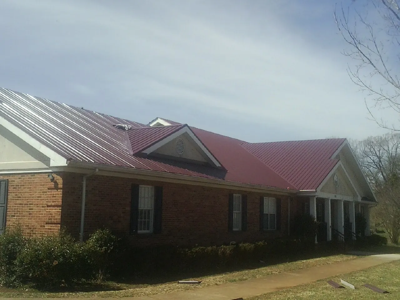 Red metal roof with gabled entries on a long brick building, from a Hail Damage Roof Repair job in Conifer