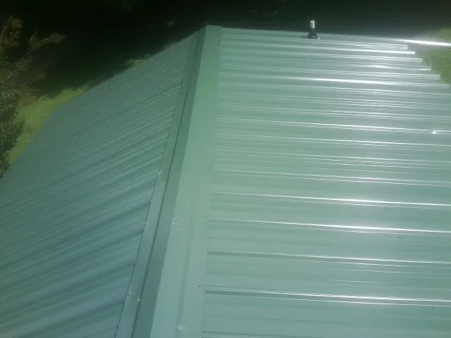 New green metal panels meeting at the ridge of a roof — Flat Roof Repair work by our crew in Conifer