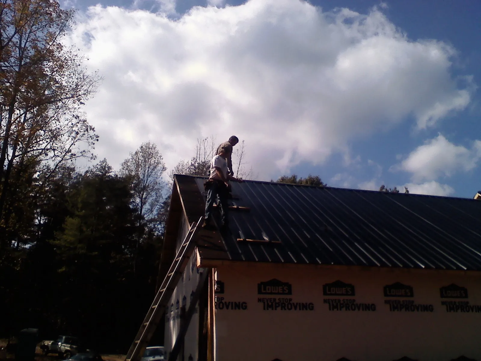 Roofer fastening dark metal panels high against a cloudy sky, from a Roof Inspection job in Conifer