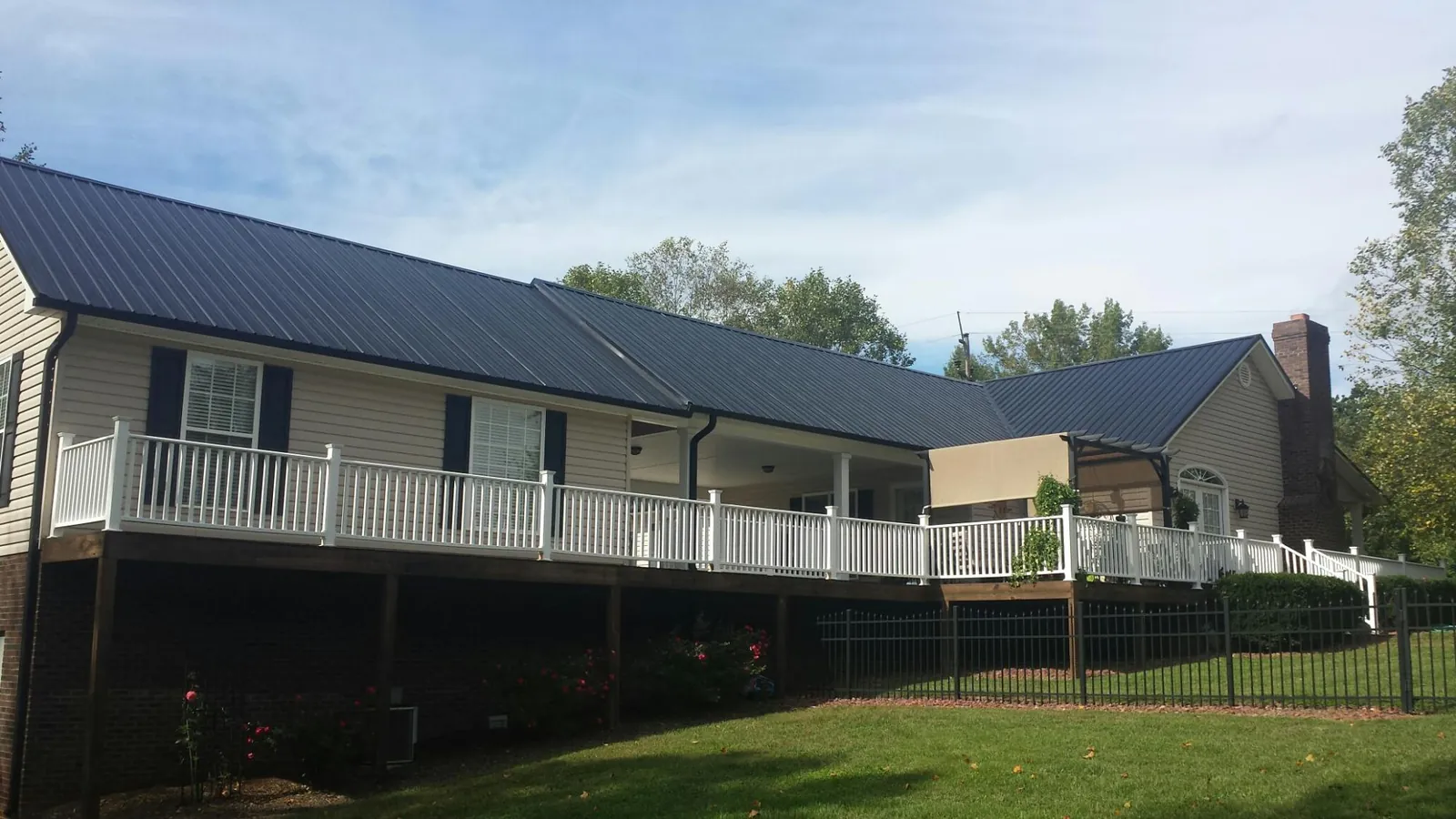 Black metal roof above a long white railed deck on a hillside home in Conifer