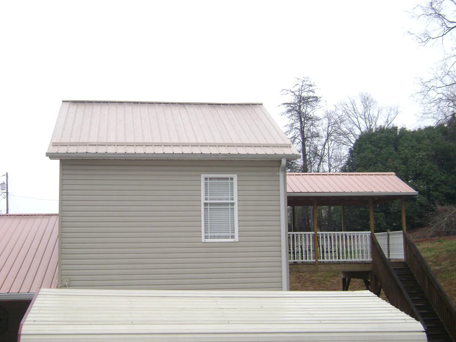 Tan metal roofs on a two story addition and attached porch, from a Roof Replacement job in Conifer